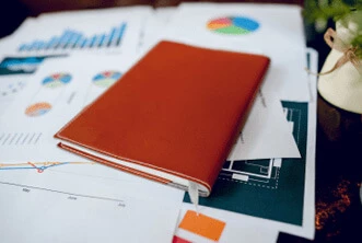 A red coloured book is placed on a table over some charts and graphs. It seems like picture is representing the service: airbnb bookkeeping service